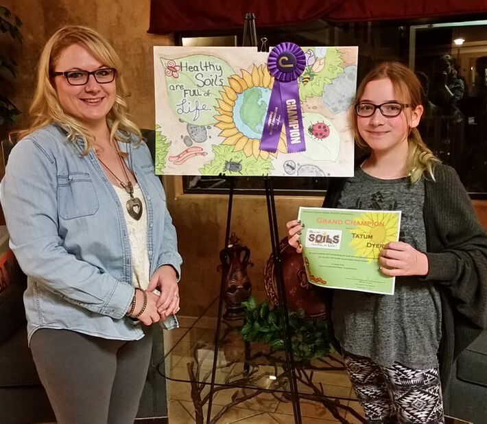6th grade Poster Contest winner shows off her grand champion ribbon and certificate, while she and her mom stand in front of her winning poster artwork